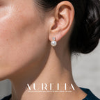 Close view of a stud with a four-prong clear accent above one round white pearl-like bead, in a gold-tone setting.