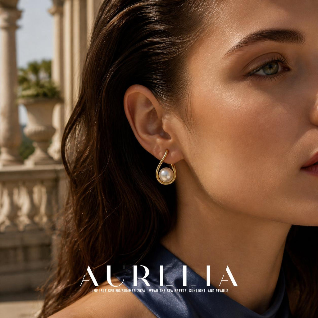 Close view of an open teardrop-shaped gold-tone earring holding a round white pearl-like bead at its lower end.