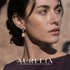 Tight ear and face view. Gold-colored round stud, one small white bead and a lower rounded rectangular plaque bearing a flower motif; matching three-part order in all worn views.