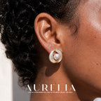 Close view of an oval whirl-shaped stud with curved white bands, gold-tone borders and a round white center.
