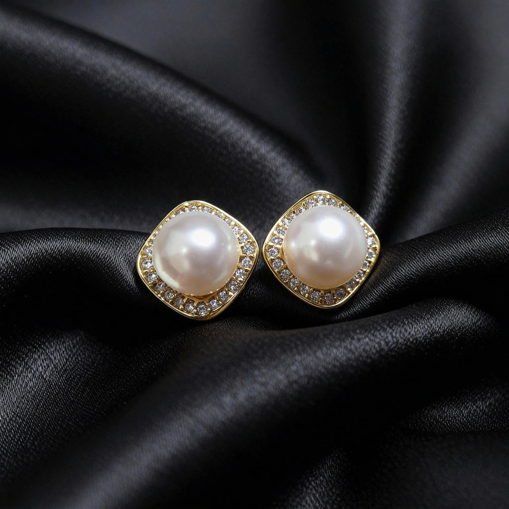 Pair of gold-tone cushion-square halo studs with round white centers, resting on black folded fabric.
