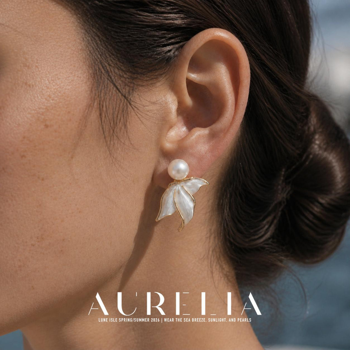 Close view of an earring worn on the ear: a white round bead above a gold-colored, three-lobed white tail motif.