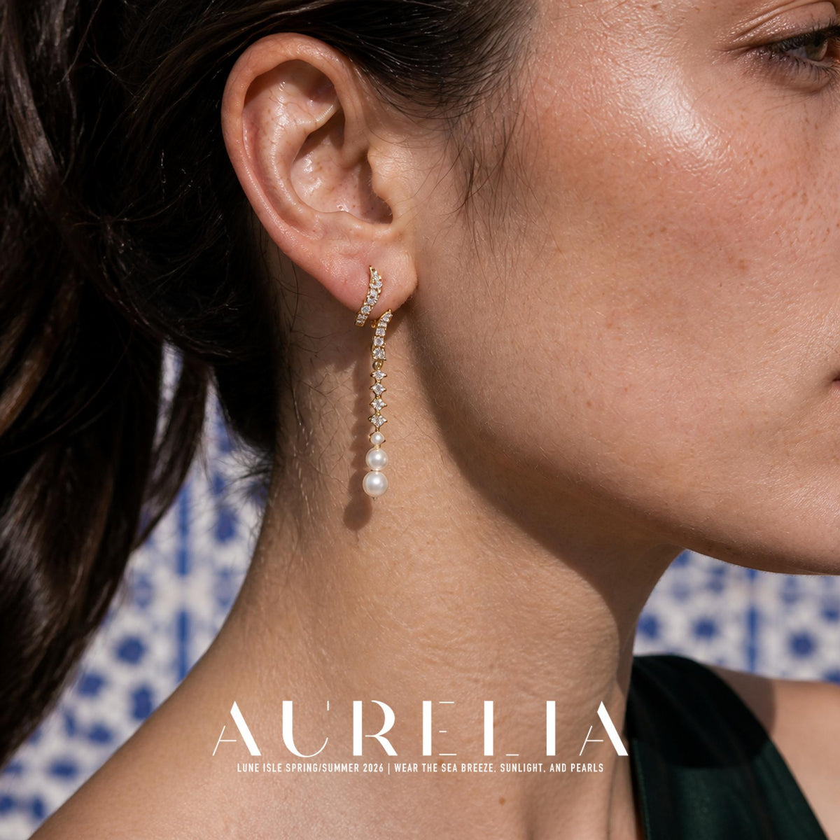 Close view of a long gold-tone drop earring with curved clear-accent upper sections, a narrow hanging row and graduated white round beads at the end.