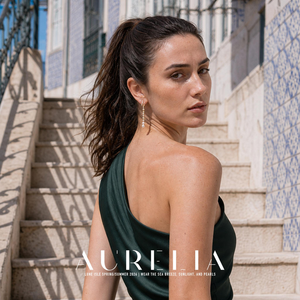 Model in a green one-shoulder outfit on stone steps, wearing the long curved gold-tone drop with white bead ends.
