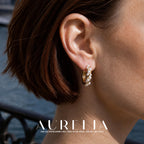 Close view of a gold-tone hoop with small white round beads following a twisting front strand.