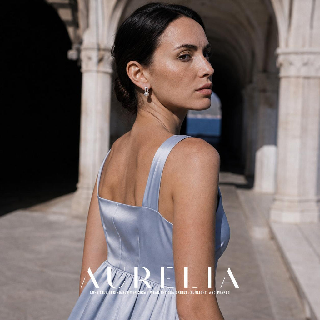 Model in a pale blue dress looking back in an arched walkway, wearing the paired-bar and white-bead earrings.