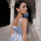 Model in a pale blue dress looking back in an arched walkway, wearing the paired-bar and white-bead earrings.