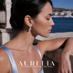Side-profile model leaning at balustrade wearing paired-bar and white-bead stud.