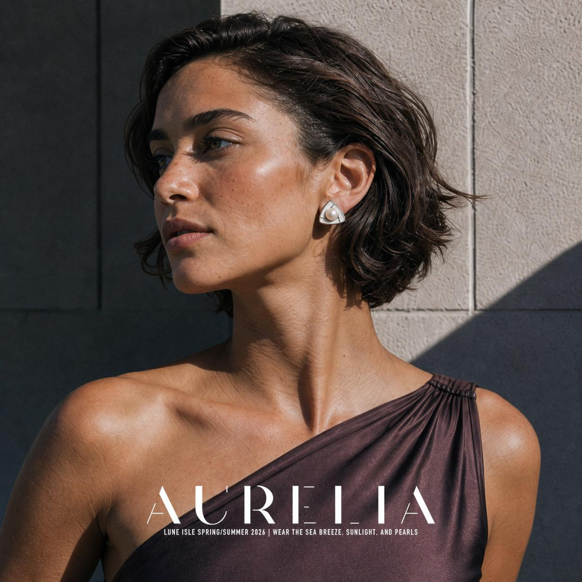 Outdoor face-and-shoulder portrait in a dark one-shoulder garment showing the triangular stud worn.