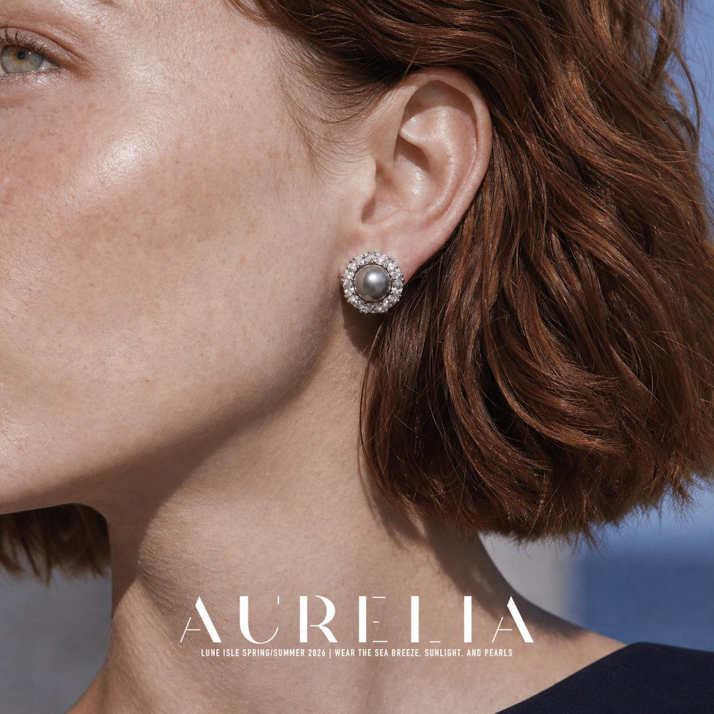 Close view of a person wearing a round silver-colored stud with a dark gray round center and a clear faceted surround; reddish hair and a dark neckline are visible.