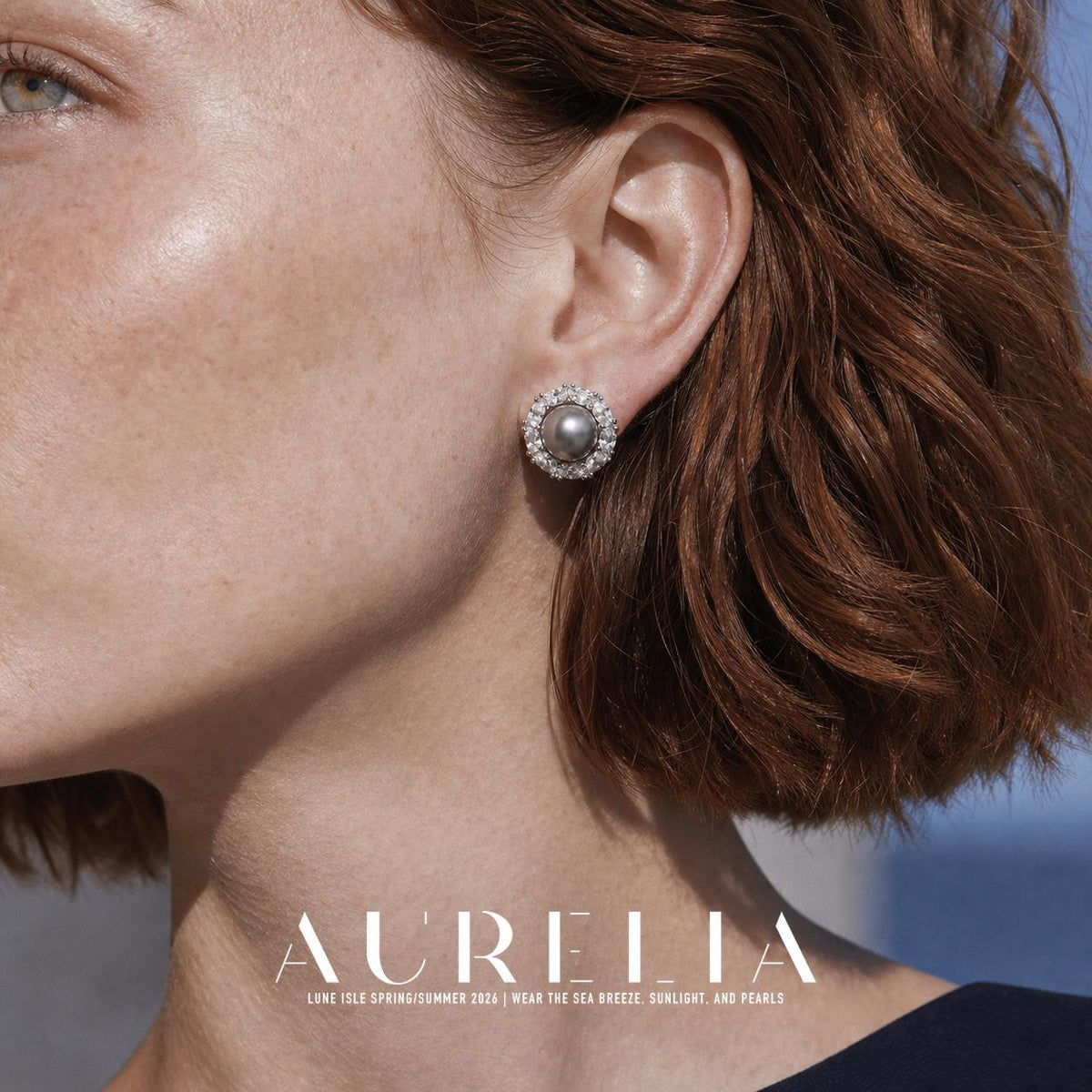 Close view of a person wearing a round silver-colored stud with a dark gray round center and a clear faceted surround; reddish hair and a dark neckline are visible.