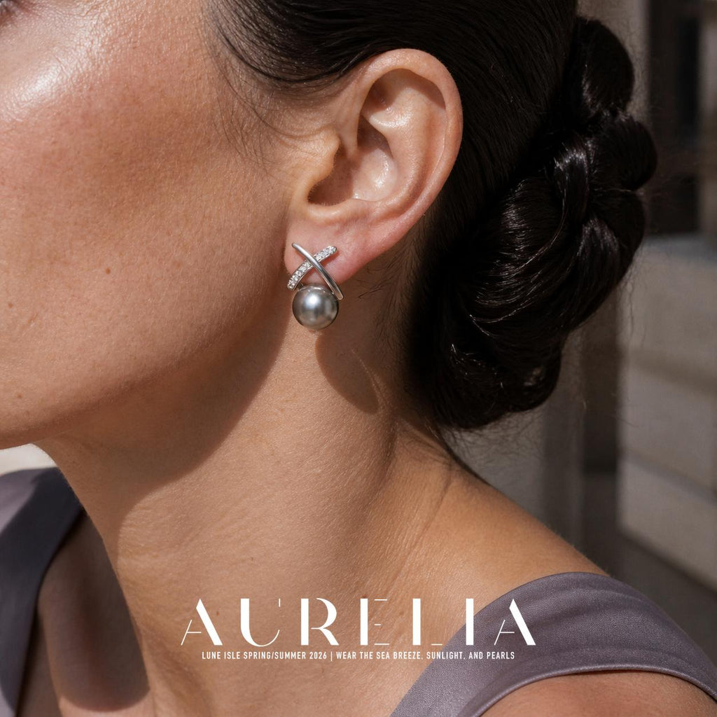 Close view of a person wearing a silver-colored earring with two crossed curved bars over a dark gray round lower element; one bar is smooth and the other has clear accents.