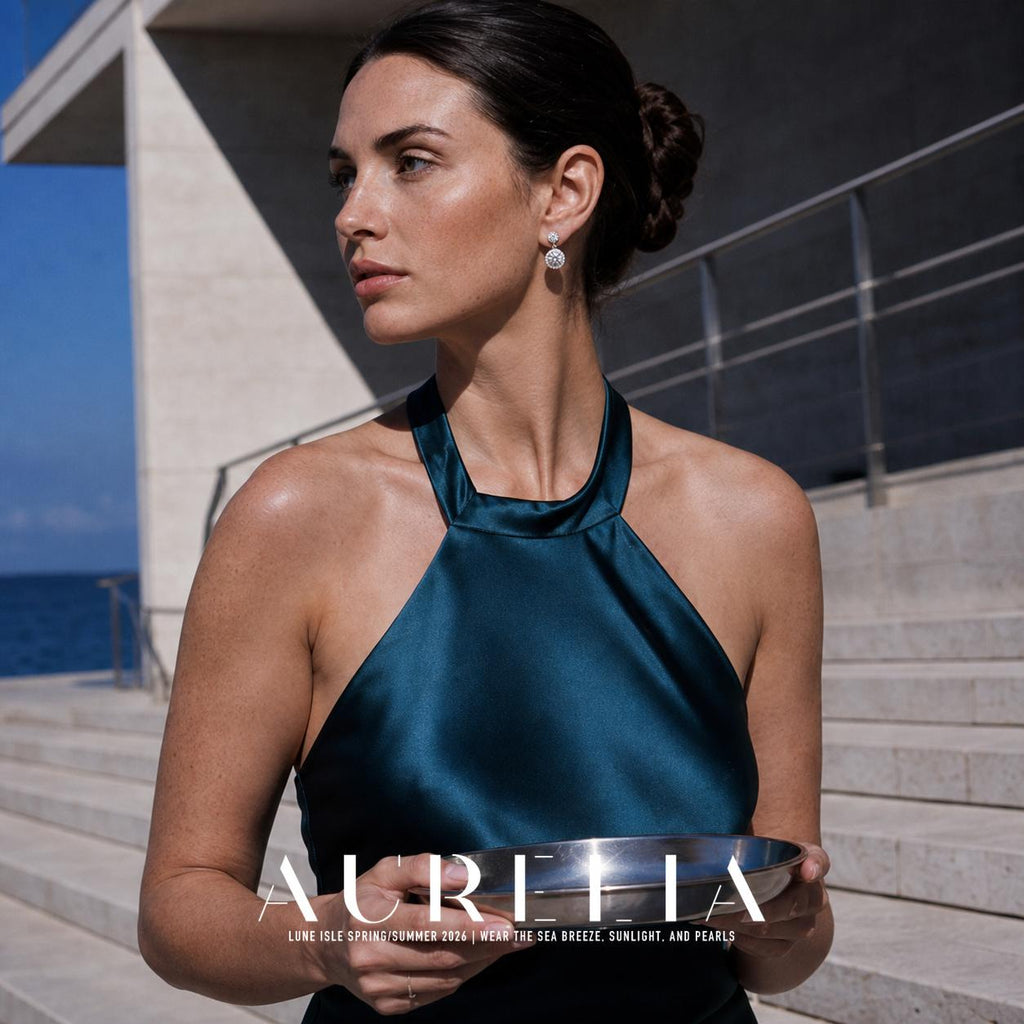 Person in a dark teal halter-neck dress holding a reflective bowl outdoors, wearing silver-colored earrings with a small round top and larger clear round drop.