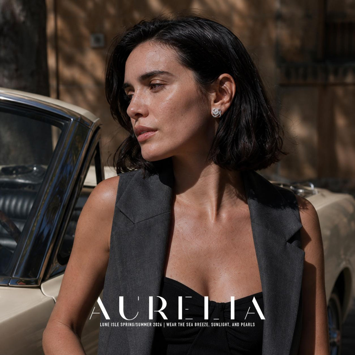Outdoor portrait beside a car showing the interlaced stud worn with a dark sleeveless jacket.