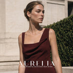 Upper-body portrait in a burgundy dress outdoors, with the single bead strand visible around the neck.