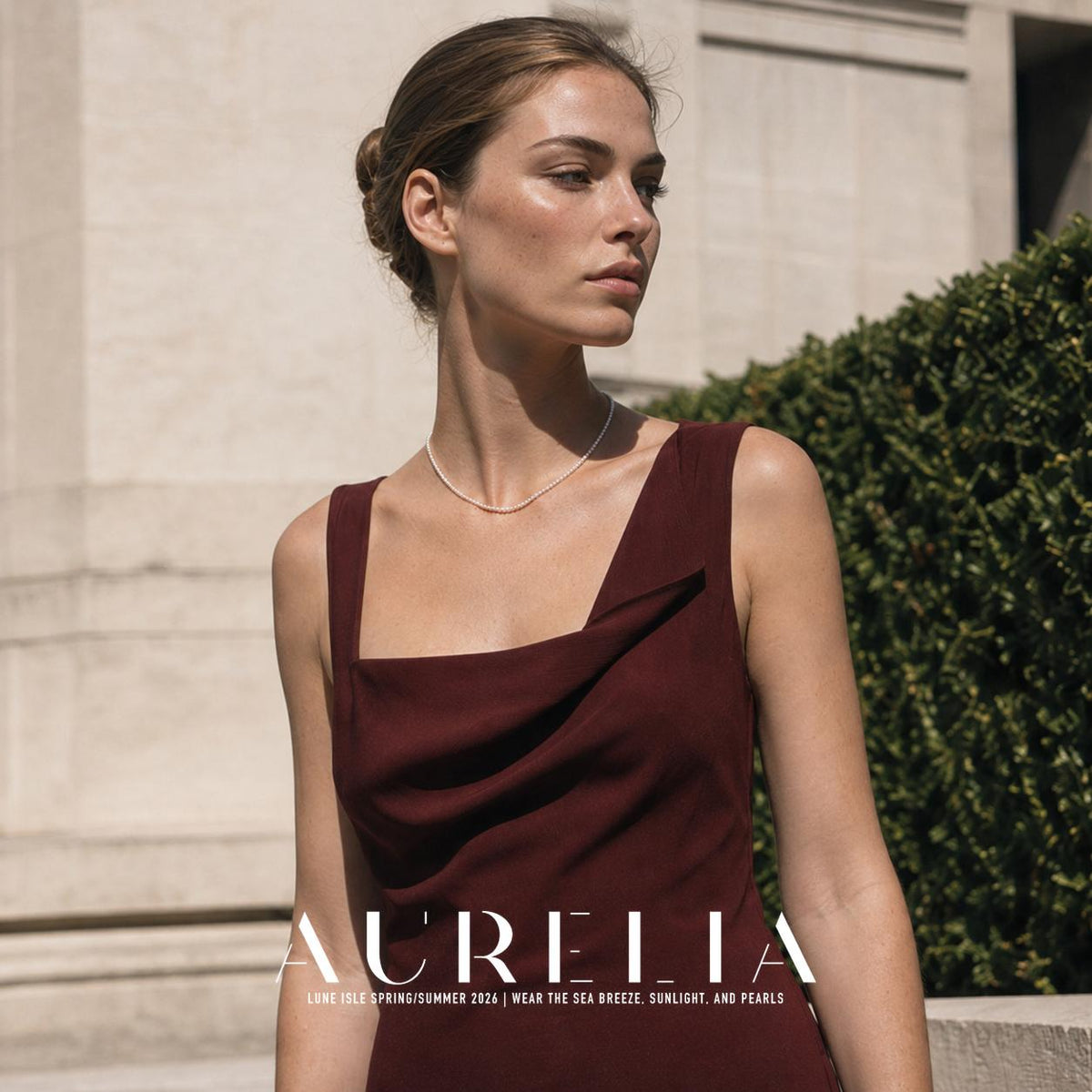 Upper-body portrait in a burgundy dress outdoors, with the single bead strand visible around the neck.