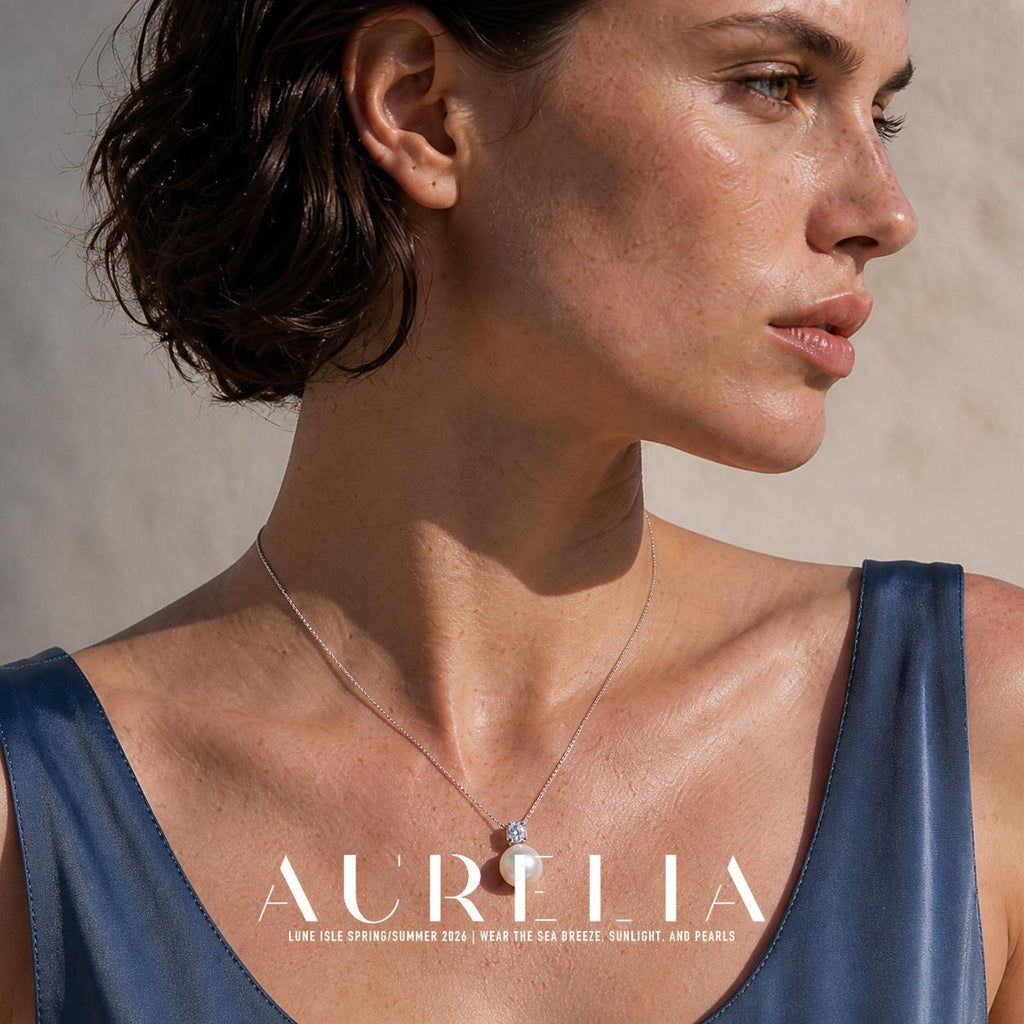 Close upper chest and face view; AURELIA lettering partly crosses the lower bead but its structure remains visible. Fine silver-colored chain joins a single clear accent above one white round pendant; all worn views retain the same small accent and round-drop order.