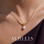 Tight on-neck view of the curved connector, central knot and white drop, with a dark plum garment at the edge.