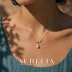 Close chest view of the fine chain, downward-pointed decorative wave and teardrop-shaped white bead.
