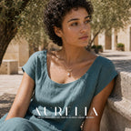 Seated courtyard portrait in teal, wearing the gold-tone wave pendant with white drop.