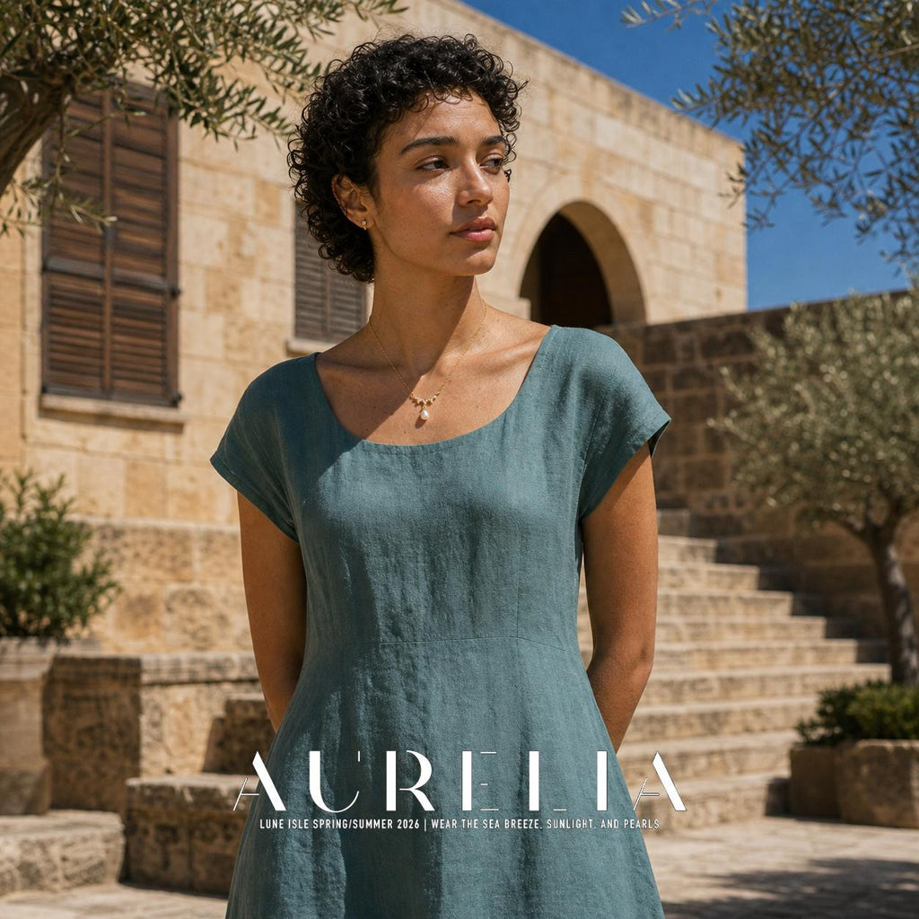 Standing portrait in teal outside a stone building; same wave and teardrop pendant visible.