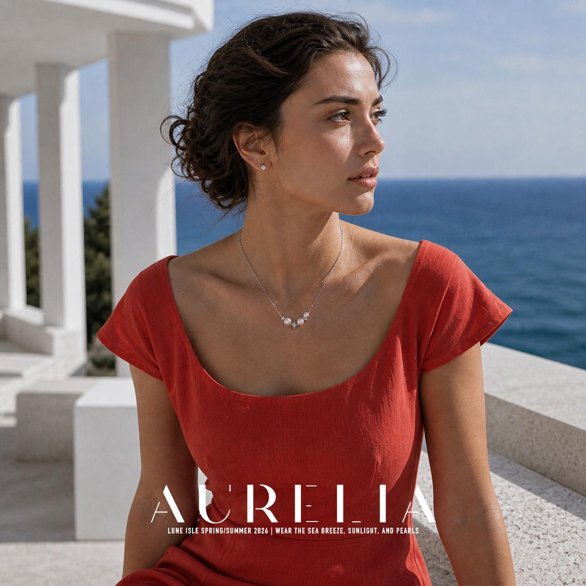 Seated upper-body portrait beside the sea, with asymmetric bead-and-star necklace unobstructed.