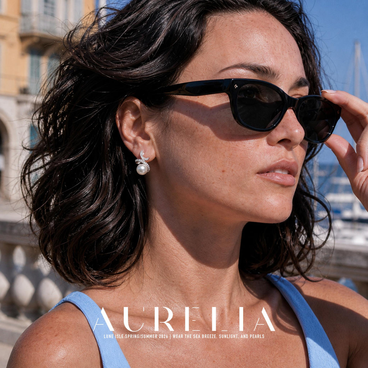 Close portrait adjusting dark sunglasses; double-swirl stone-set earring fully visible.