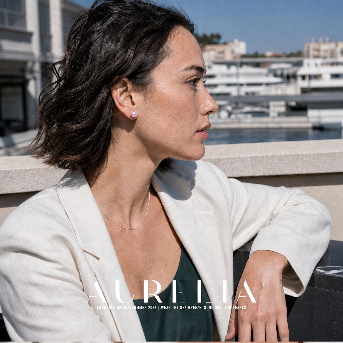 Side portrait of a model in a pale jacket at a marina, wearing the pink stud.
