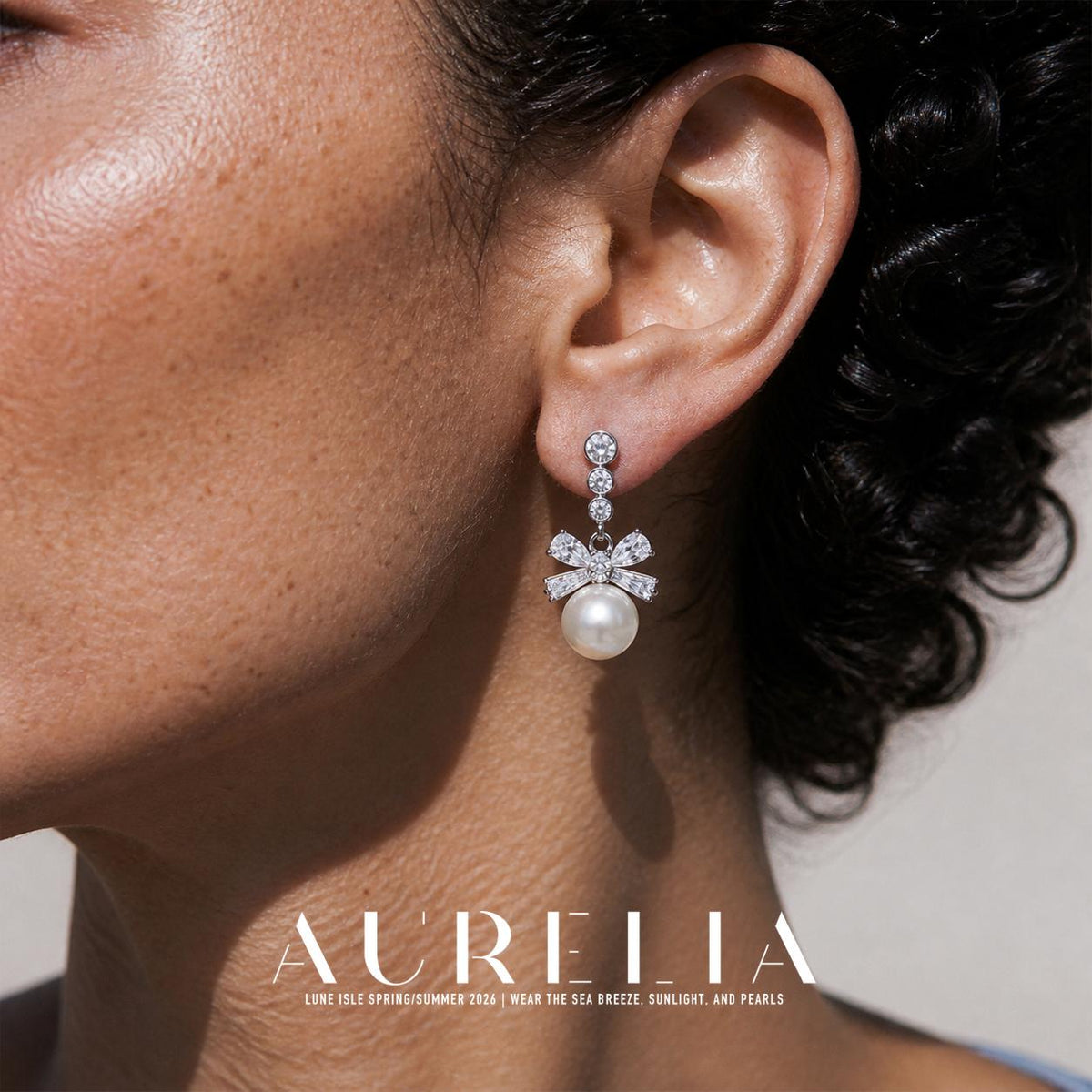 Close view of a person wearing a silver-colored earring with three descending round clear accents, a bow-shaped clear-accent arrangement and a white round bottom drop.