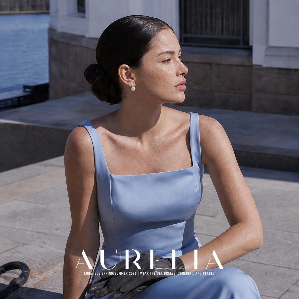 Seated outdoor portrait in pale blue, showing the twin-arc white-bead earring.