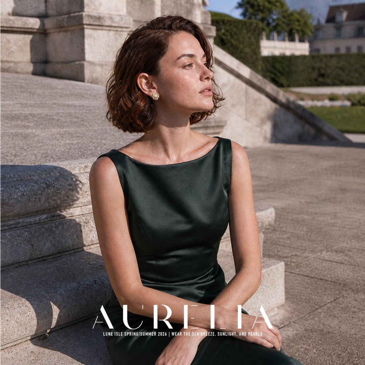 Seated portrait on stone steps in dark green, floral stud visible at ear.