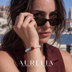 Model adjusting sunglasses, bracelet visible. White bead strand with one larger red round accent, two turquoise-colored disc spacers and a silver-colored spacer; all worn views preserve this arrangement.